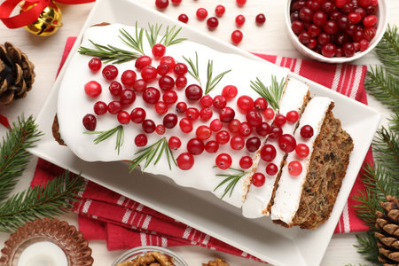 Tasty Christmas cake with icing, cranberries, rosemary and festive decor on white wooden table, flat layの写真素材