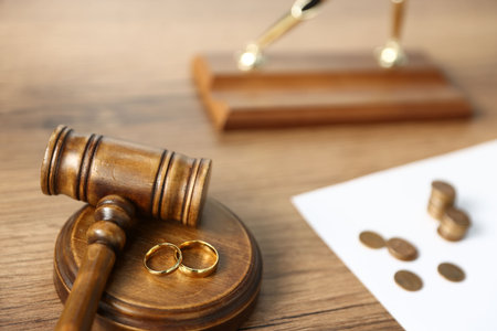 Alimony. Judge's gavel, engagement rings, sheet of paper and coins on wooden table, selective focusの写真素材