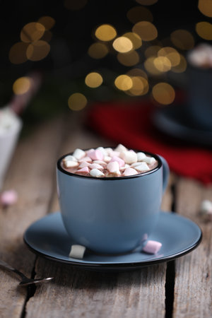 Tasty cocoa with marshmallows on wooden table against blurred Christmas lights, closeupの写真素材