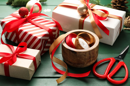 Festive packaging. Gift boxes, ribbons, scissors, wrapping paper and Christmas decor on green wooden table, closeupの写真素材