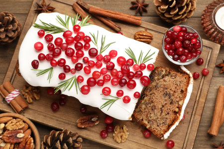 Tasty Christmas cake with icing, cranberries and rosemary on wooden table, flat layの写真素材