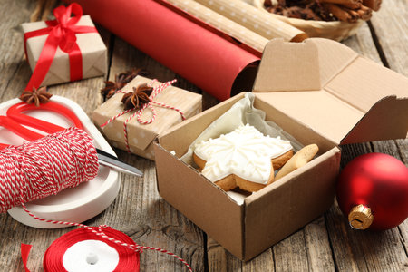 Festive packaging. Gift boxes, wrapping paper, twine, scissors, cookies and bauble on wooden table, closeup. Merry Christmas and Happy New Yearの写真素材