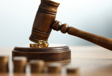 Alimony. Judge's gavel, engagement rings and coins on wooden table against gray background, selective focusの写真素材