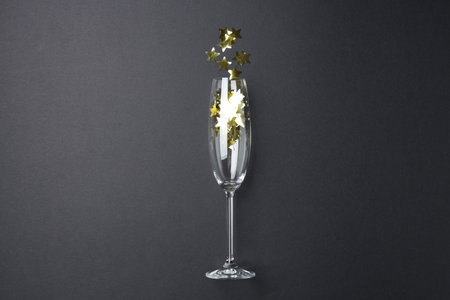 Flute glass with golden star shaped confetti on black background, top viewの写真素材