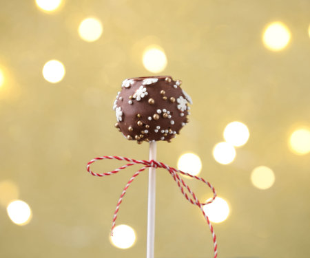Tasty cake pop on beige background with blurred lights, closeup.の写真素材