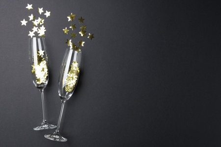 Flute glasses with golden star shaped confetti on black background, flat lay. Space for textの写真素材