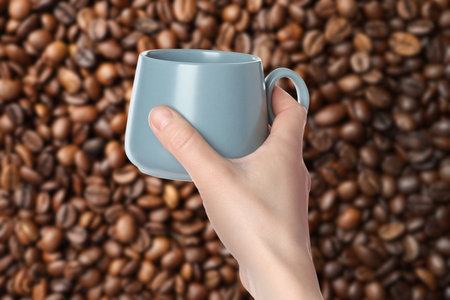 Woman holding gray cup against roasted coffee beans, closeupの写真素材