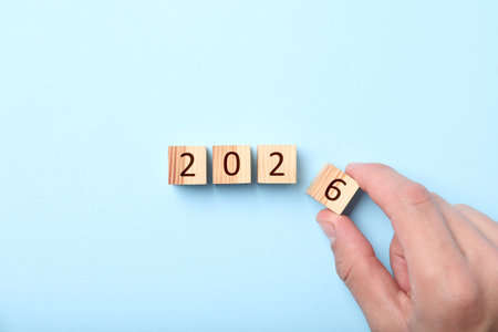 Man putting cube with number 6 on light blue background, top view