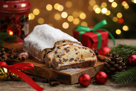 Traditional Christmas Stollen with icing sugar, spices and festive decor on wooden table against blurred lights, closeup. Bokeh effectの写真素材
