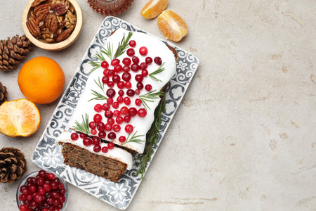 Tasty Christmas cake with icing, cranberries, nuts, and festive decor on light gray table, flat lay....
