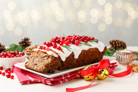Tasty Christmas cake with icing, cranberries and rosemary on white wooden table against background...