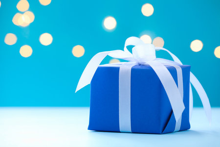 Beautiful gift box on white table against light blue background with blurred lights, closeup with space for text. Bokeh effectの写真素材