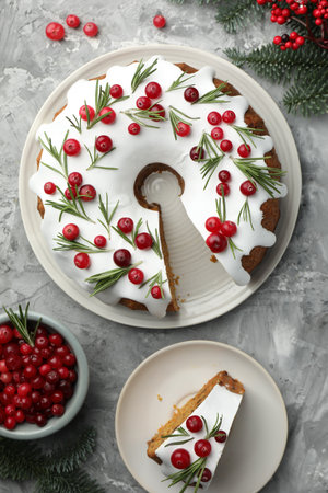 Delicious cut Christmas cake with icing, cranberries, rosemary and fir tree branches on gray...