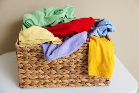 Wicker basket with laundry on white table near beige wall indoors, closeup