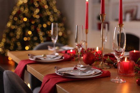 Stylish Christmas table setting with plates, glasses and burning candles in festive decorated room, closeupの写真素材
