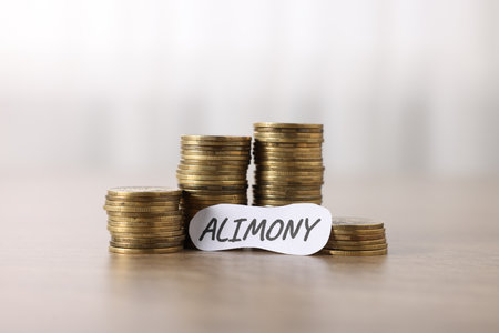 Paper note with word Alimony and stack of coins on wooden table, closeupの写真素材