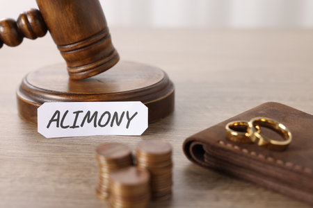 Paper note with word Alimony, judge's gavel, coins, wallet and wedding rings on wooden table, closeupの写真素材