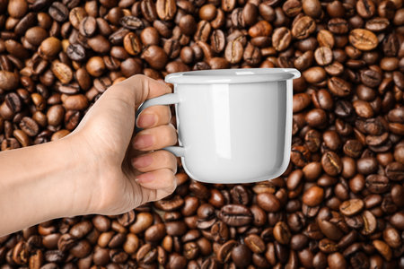 Woman holding white cup against roasted coffee beans, closeupの写真素材