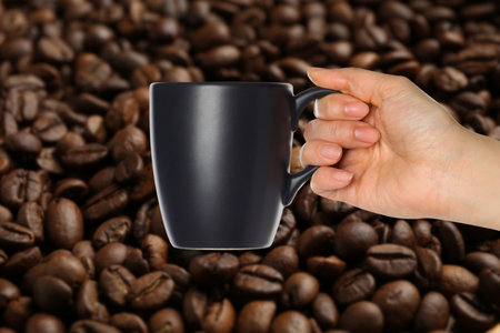 Woman holding black cup, closeup. Roasted coffee beans on backgroundの写真素材