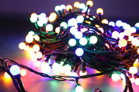 Bright Christmas lights on table in darkness, closeup. New Year greeting card
