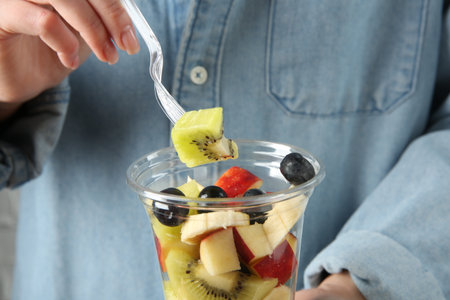 Woman eating tasty fruit salad from plastic cup, closeup. Healthy snackの写真素材