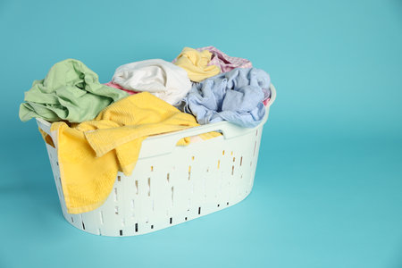 Laundry basket with clothes on light blue background, space for textの写真素材