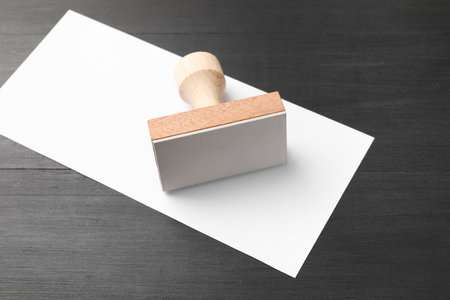 One wooden stamp and blank sheet of paper on black table, closeup. Space for textの写真素材