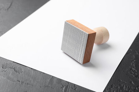 One wooden stamp and blank sheet of paper on dark textured table, closeup. Space for textの写真素材