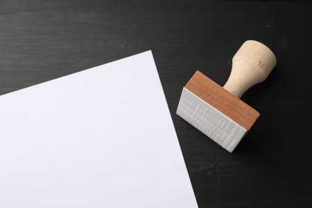 One wooden stamp and blank sheet of paper on black table, top view. Space for textの写真素材