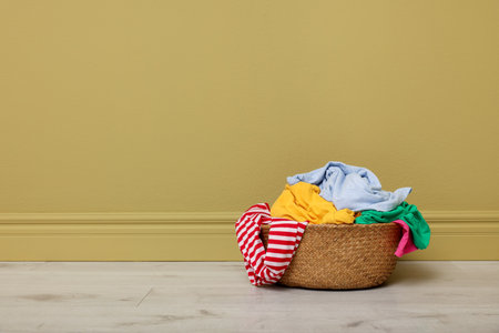 Wicker basket with laundry near yellow wall indoors, space for textの写真素材