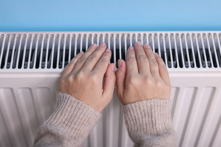 Woman warming her hand near radiator indoors, above viewの写真素材