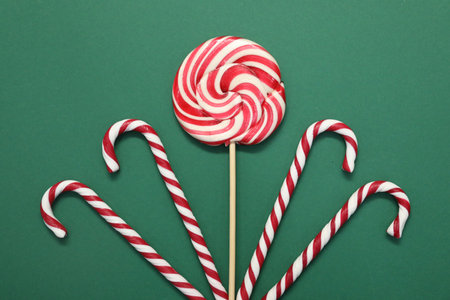 Christmas treat. Lollipop and candy canes on green background, top view