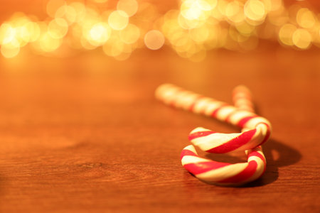 Merry Christmas and Happy New Year. Tasty candy canes on wooden table against blurred lights,...