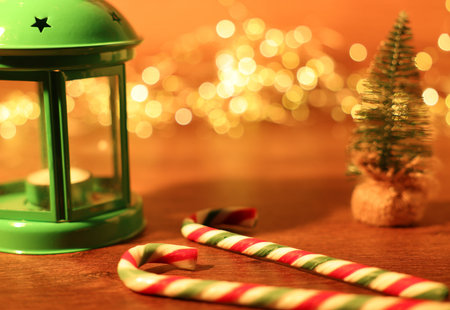 Tasty candy canes, lantern and Christmas decor on wooden table against blurred lights, closeup