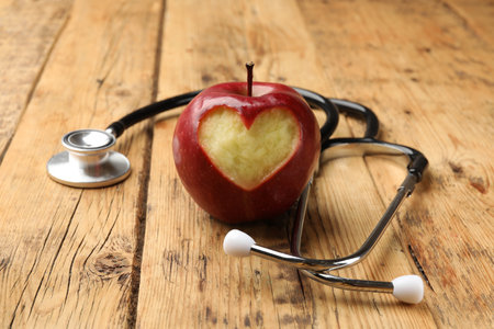 Apple with carved heart and stethoscope on wooden table, closeupの写真素材