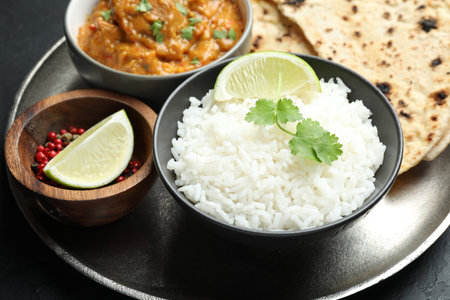 Delicious rice, lime, cilantro, and peppercorns on dark textured table, closeup