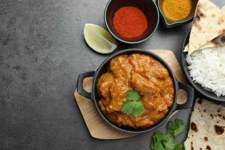Delicious chicken tikka masala, rice, cilantro, lime, lavash and spices on gray textured table, flat lay. Space for textの写真素材