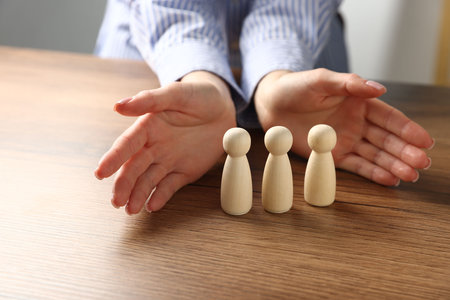 Woman protecting human figures at wooden table, closeupの写真素材