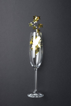 Flute glass with golden star shaped confetti on black background, top viewの写真素材
