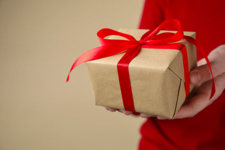 Woman with gift box on beige background, closeup. Space for text
