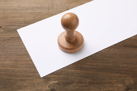 One wooden stamp and blank sheet of paper on table, closeup. Space for text