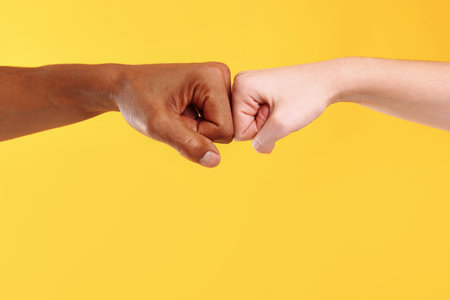 African American man bumping fists with his partner on yellow background, closeup.の写真素材