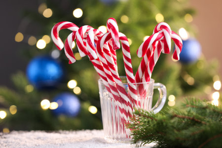 Candy canes in mug and Christmas decor on table against blurred lightsの写真素材