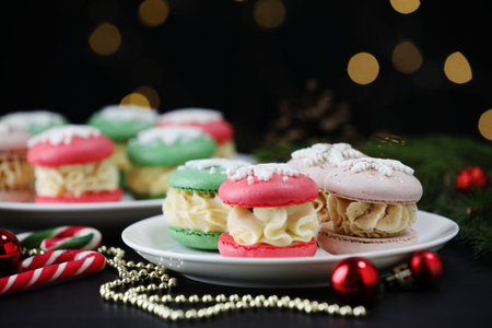 Tasty macarons and Christmas decor on black table against blurred lights, closeupの写真素材