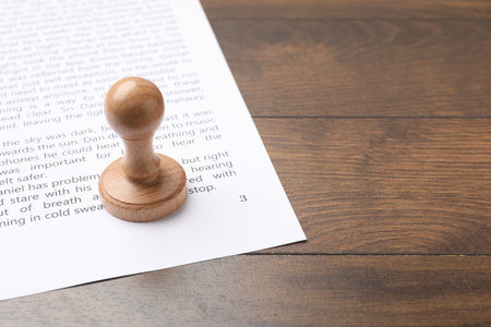 One wooden stamp and sheet of paper with text on table, closeup. Space for textの写真素材