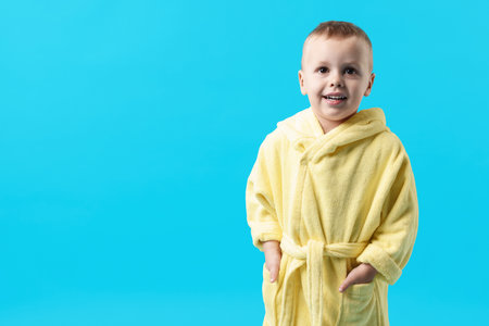 Smiling little boy in yellow bathrobe on light blue background. Space for textの写真素材