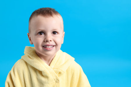 Smiling little boy in yellow bathrobe on light blue background. Space for textの写真素材