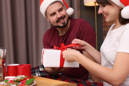 Happy couple in pajamas with Christmas gift and snacks in roomの写真素材