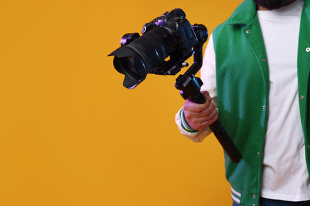 Videographer using gimbal stabilizer with camera on yellow background, closeup. Space for text
