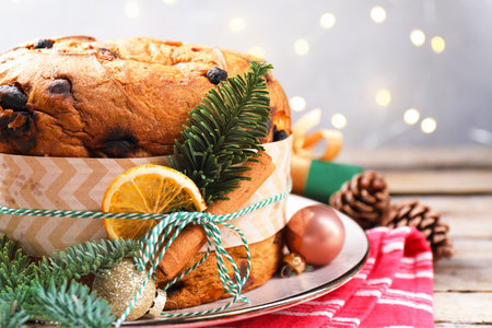 Tasty panettone cake with spices and Christmas decor on wooden table against gray background with blurred lights, closeup. Space for textの写真素材